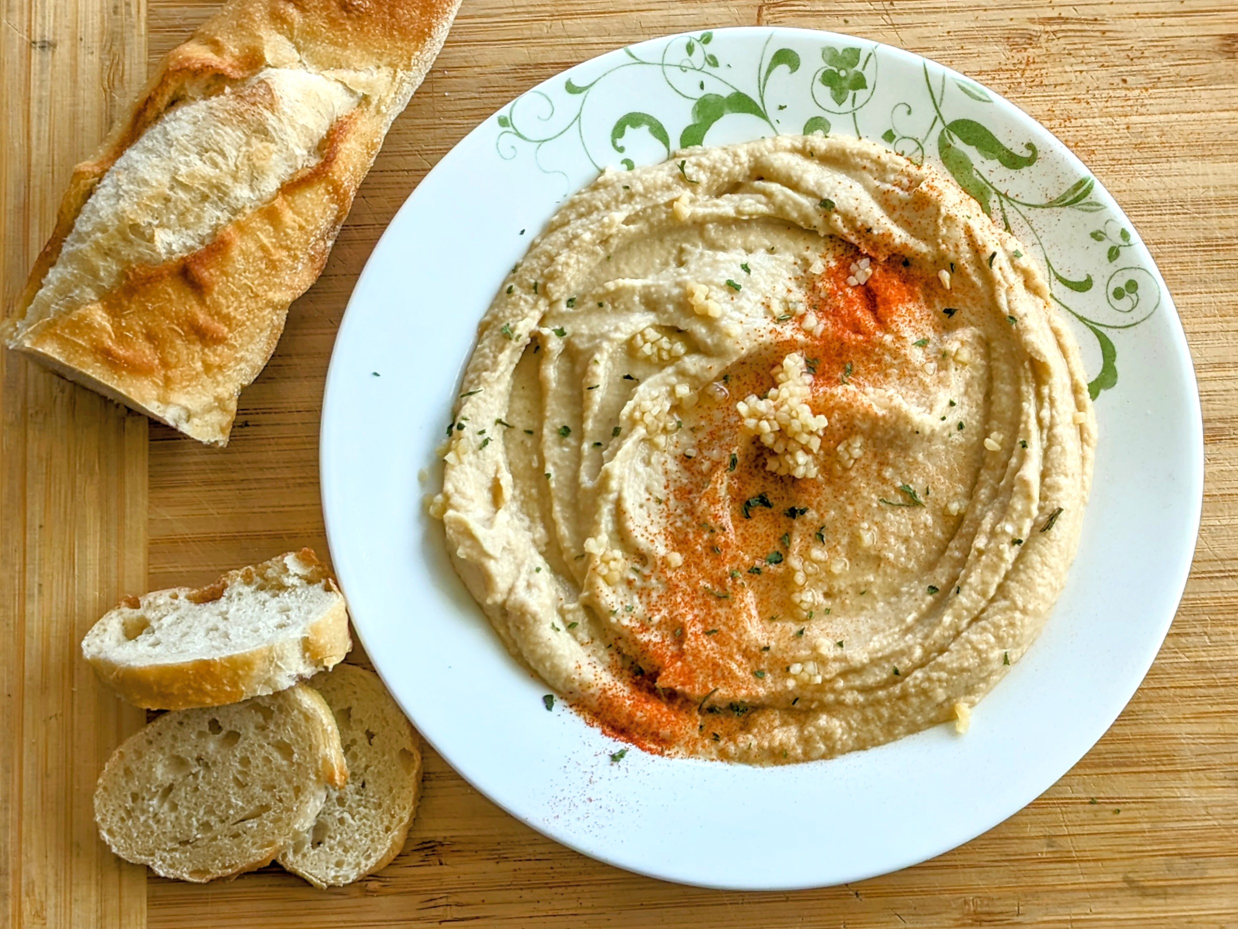 Photograph of the BEST hummus ever dusted in paprika, parsley, and minced garlic with baguette