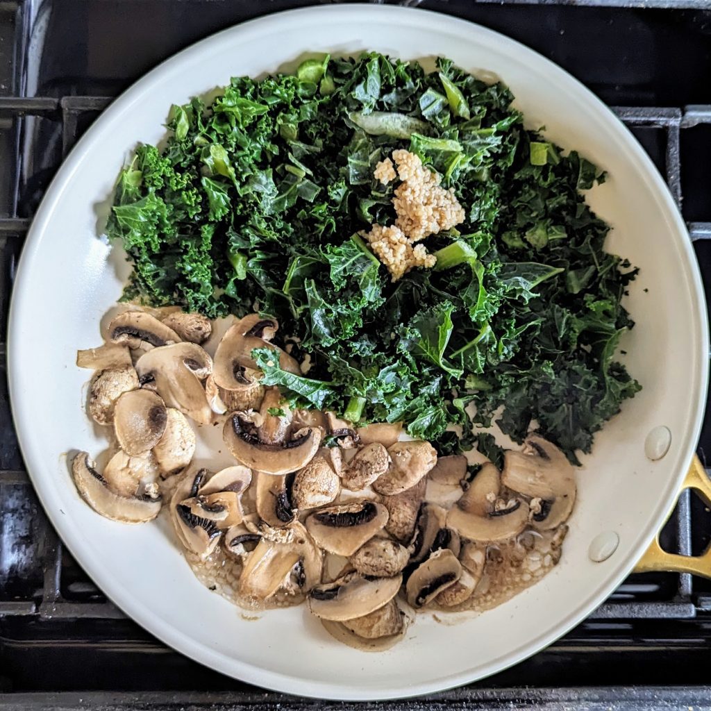 The Mighty KMG: Kale, Mushrooms, and Garlic in a skillet as they initially cook with garlic on the kale and mushrooms on the other side